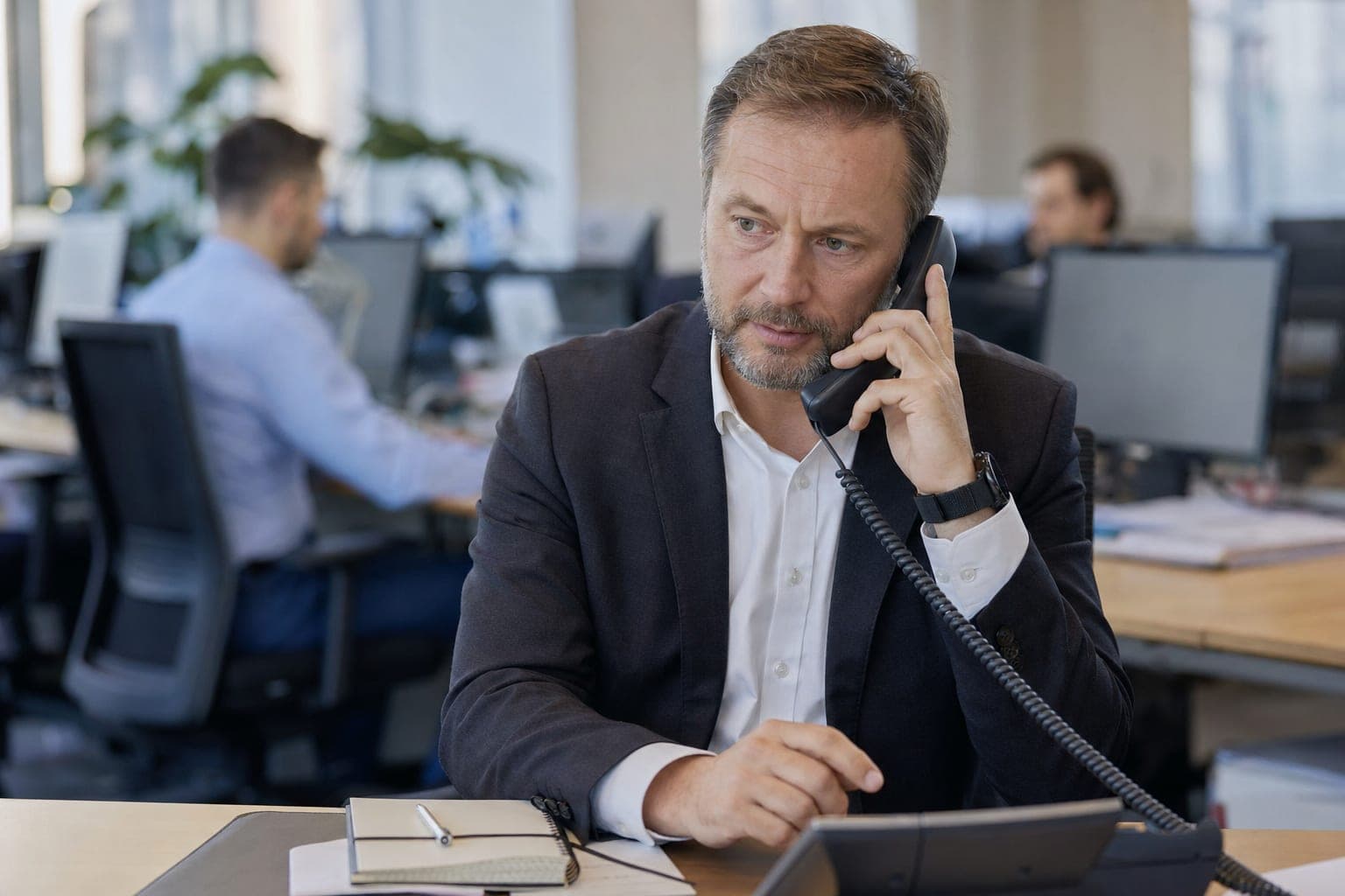 Recruiter im Büro am Telefon, daneben Notizblock und Tischapparat